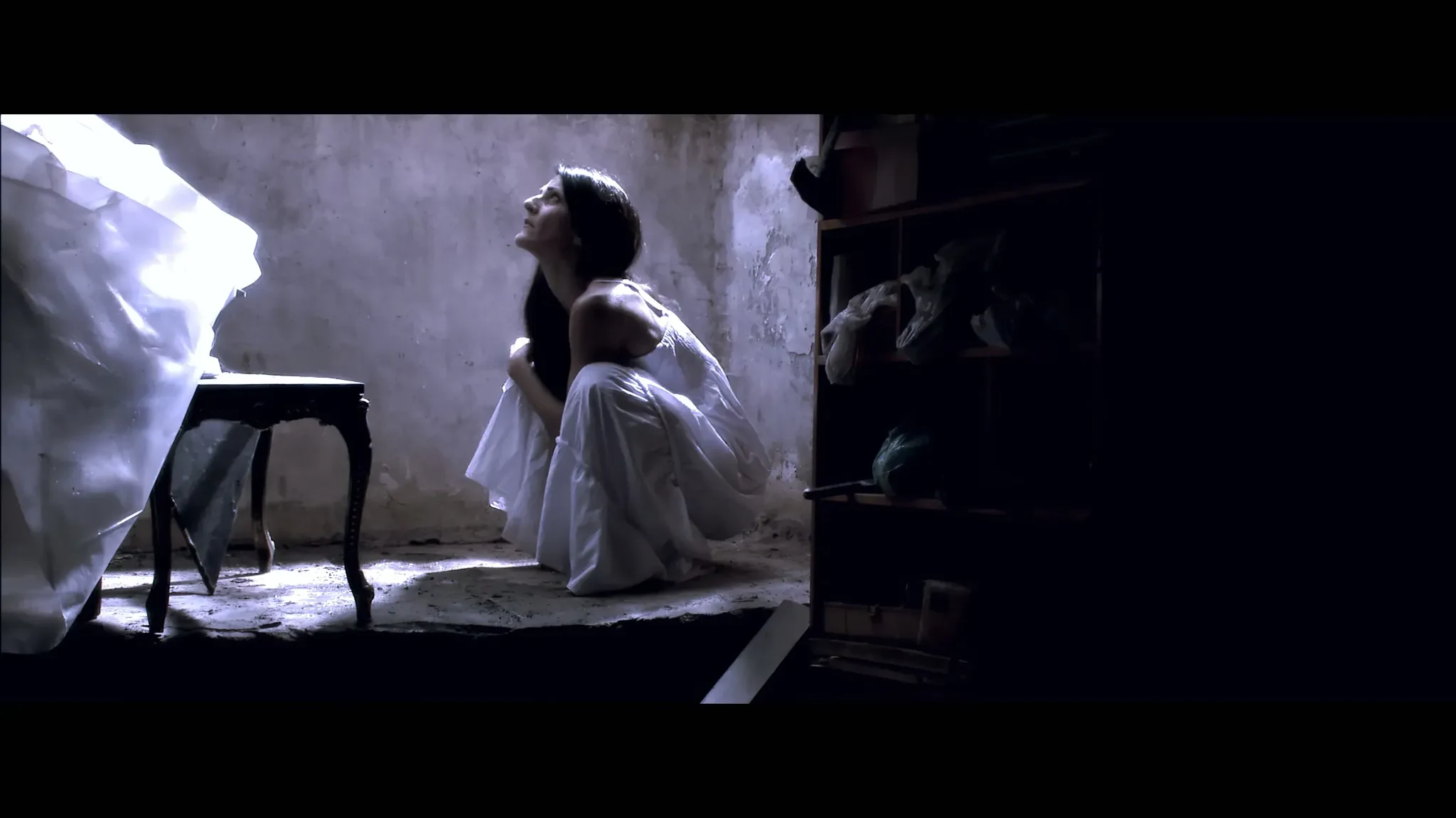 Sotiria still of woman in white dress crouched in a ruined interior lit from above